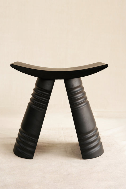 Black stool with curved top and thick legs on a beige background