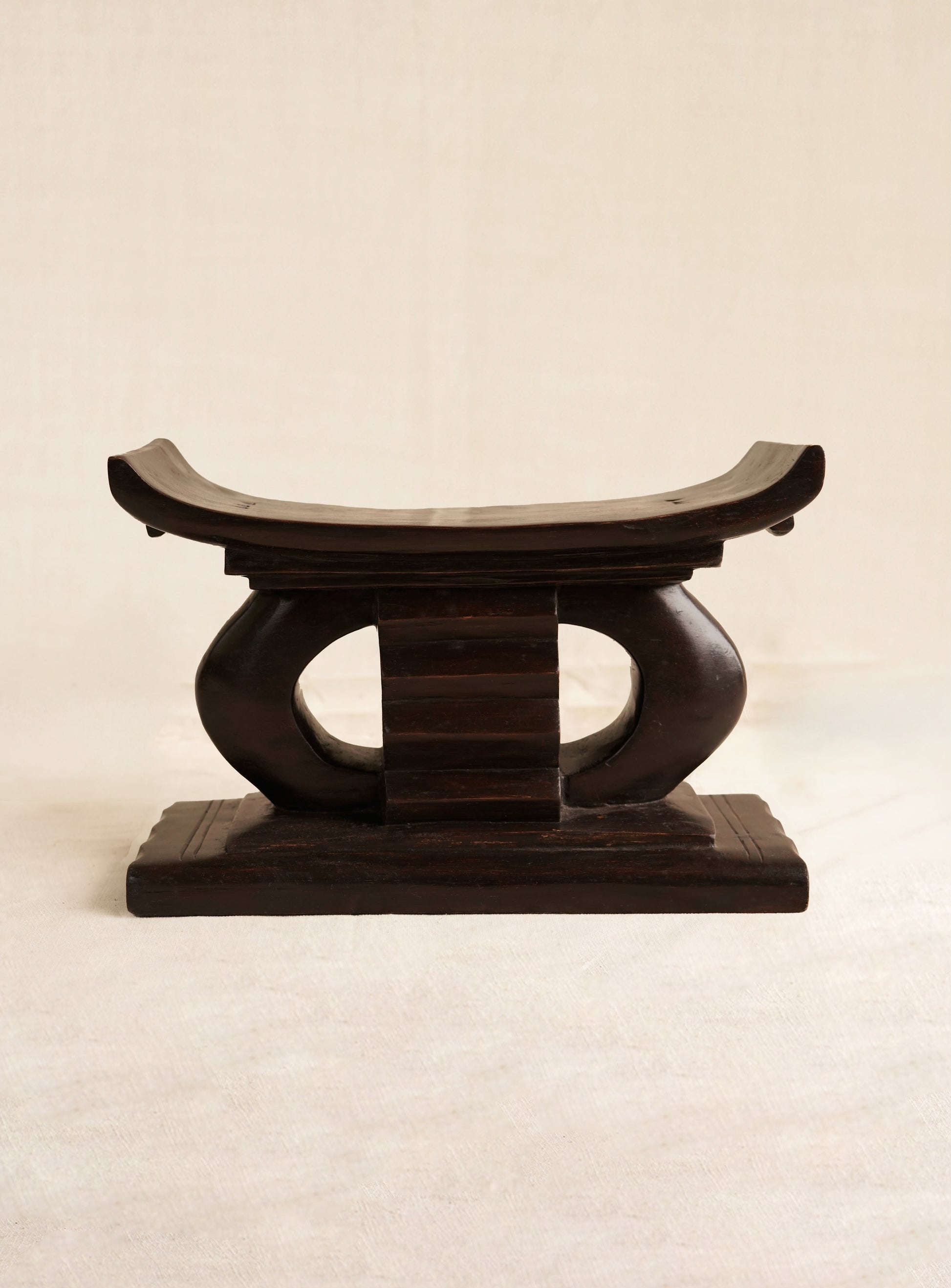 Miniature Wooden Ashanti stool with curved design on a beige background