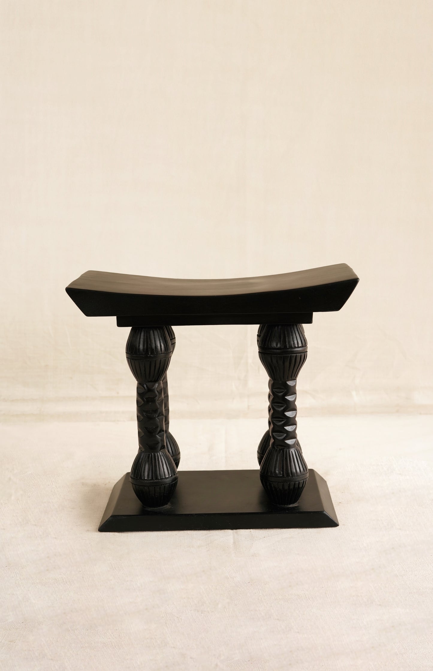 Black wooden stool with braided legs on a beige background