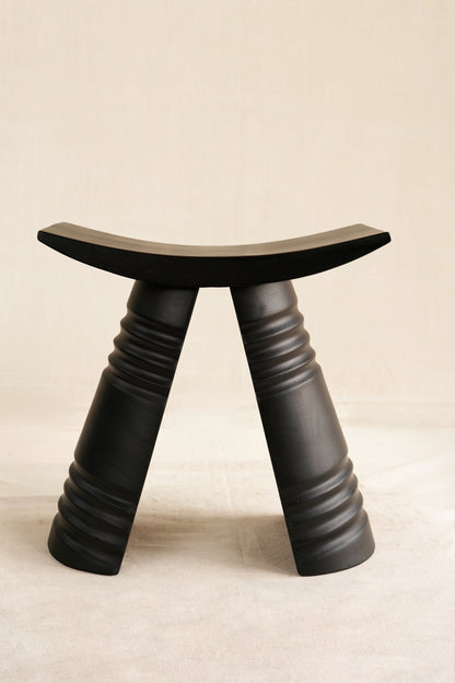Black stool with curved top and thick legs on a beige background