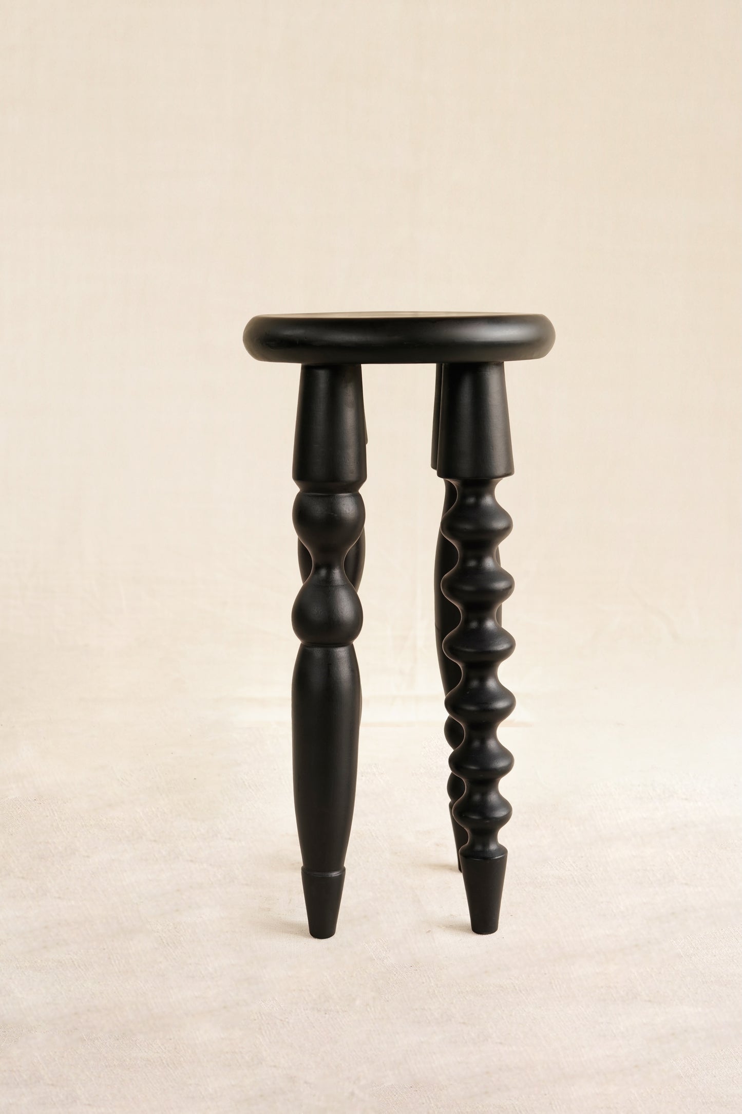 Black wooden stool with twisted legs on a beige background