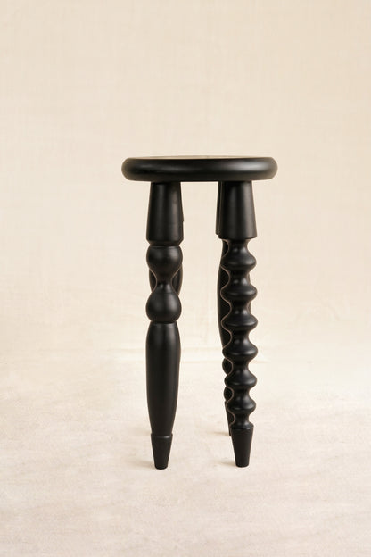 Black wooden stool with twisted legs on a beige background